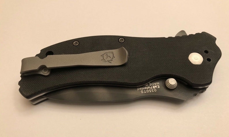 Puede incluir: Cuchillo de bolsillo negro con una pinza plateada y un tornillo plateado. El cuchillo tiene el texto "03501S KAI Patented MADE IN" en el lateral.