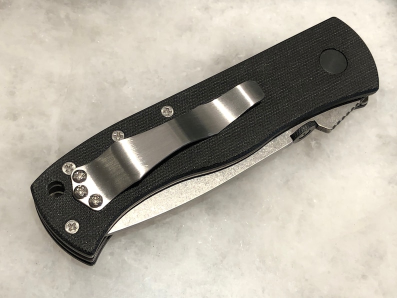 May include: A black pocket knife with a stainless steel clip and a black handle. The knife has a partially serrated blade.