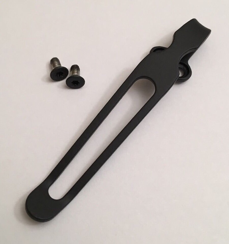 May include: Black metal pocket clip with two screws. The clip has a rounded end and a long, narrow opening.