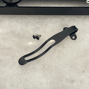 May include: Black metal pocket clip with two screws. The clip is designed to attach to a pocket or belt.