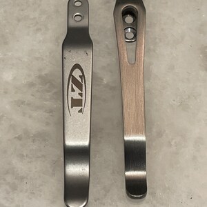 May include: Two silver metal pocket clips. The clip on the left has the text "ZT" in a circle.