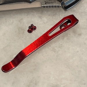 May include: A red metal pocket clip with two small screws. The clip is designed to attach to a pocket knife.