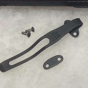 May include: Black titanium pocket clip with a small oval-shaped piece with two holes. The clip has a small inscription in Japanese characters. Three small screws are also included.