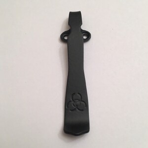 May include: Black metal pocket clip with a biohazard symbol engraved on the front.