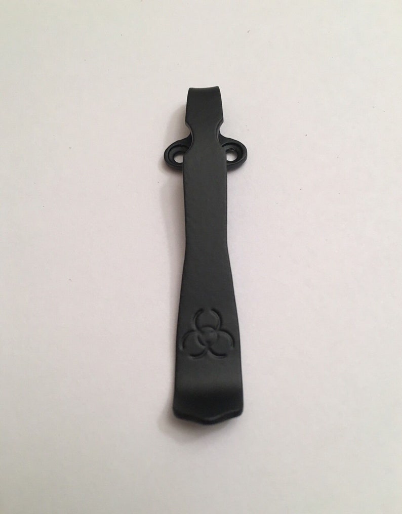 May include: Black metal pocket clip with a biohazard symbol engraved on the front.