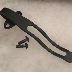 May include: Black metal pocket clip with two screws. The clip is designed to attach to a pocket knife or other tool.