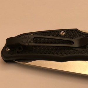 May include: Black pocket knife with a textured black handle and a silver blade. The knife has a pocket clip and the text "ERCO DURAA" is visible on the handle.