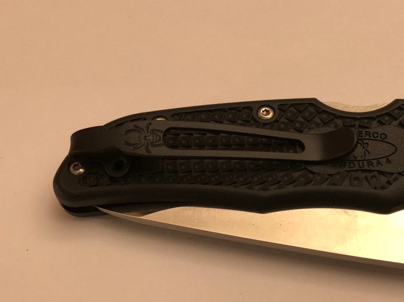 May include: Black pocket knife with a textured black handle and a silver blade. The knife has a pocket clip and the text "ERCO DURAA" is visible on the handle.