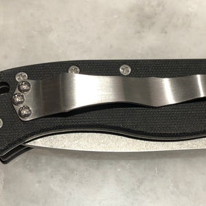 May include: A black pocket knife with a stainless steel clip and a textured black handle.