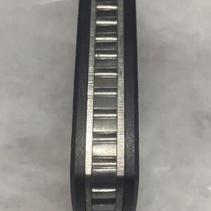 May include: Close-up of a black and silver pocket knife handle with a textured pattern.