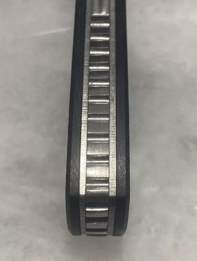 May include: Close-up of a black and silver pocket knife handle with a textured pattern.
