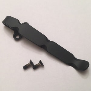 May include: Black metal pocket clip with two screws. The clip has a curved design and a hole at the top.