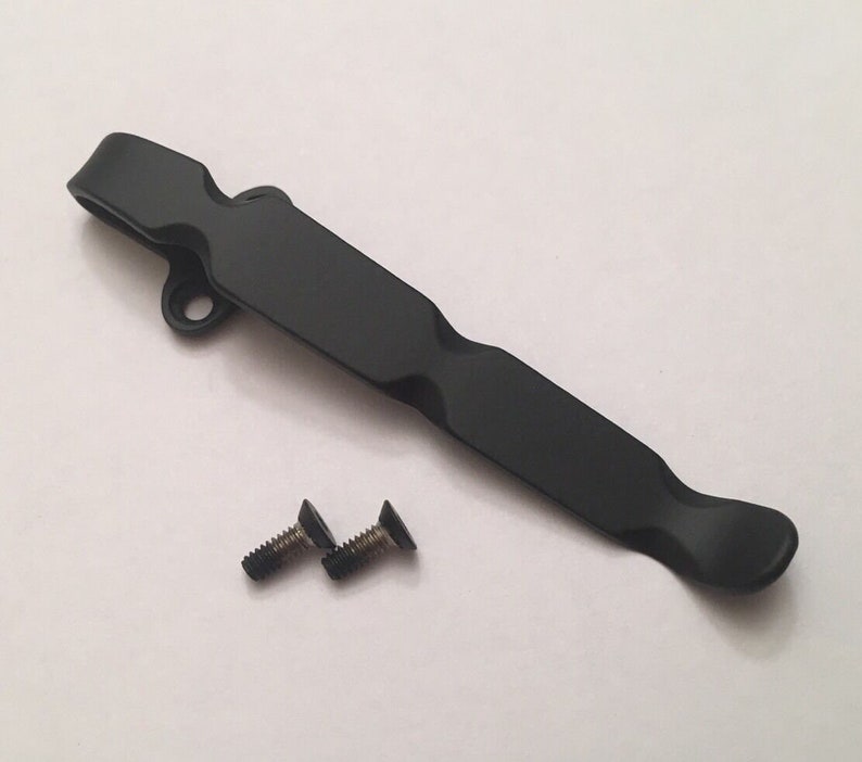 May include: Black metal pocket clip with two screws. The clip has a curved design and a hole at the top.