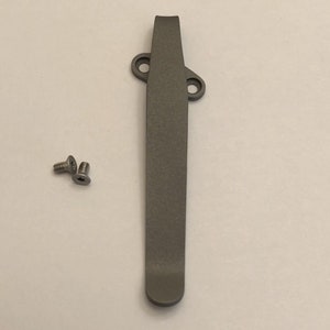 May include: A gray titanium pocket clip with two screws. The clip is designed to attach to a pocket knife or other tool.