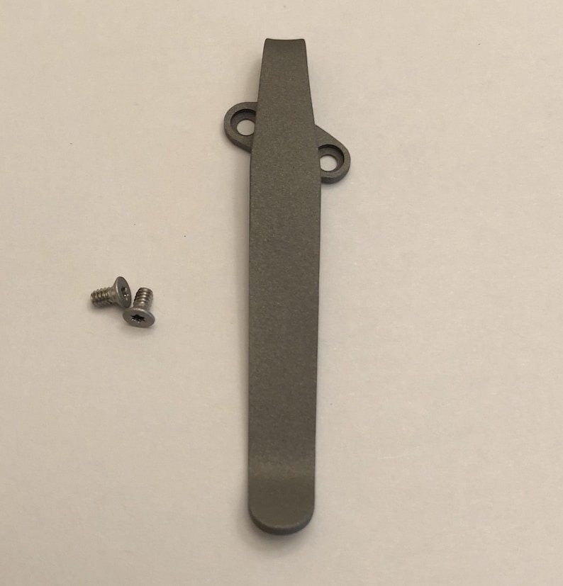 May include: A gray titanium pocket clip with two screws. The clip is designed to attach to a pocket knife or other tool.