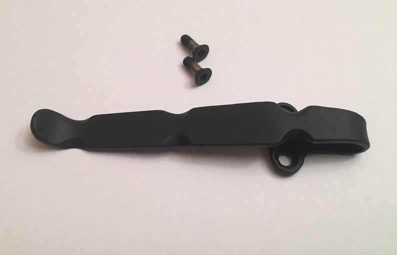 May include: Black metal pocket clip with two screws. The clip has a rounded end and a hole for attaching to a belt or bag.
