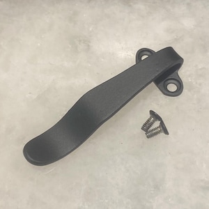 Puede incluir: Clip de bolsillo de metal negro con dos tornillos. El clip es curvo y tiene un acabado liso.