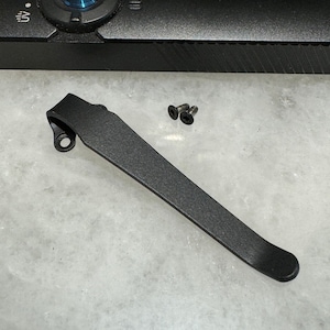 May include: A black metal hook with a rounded end and a small hole near the top. Two small silver screws are also included.