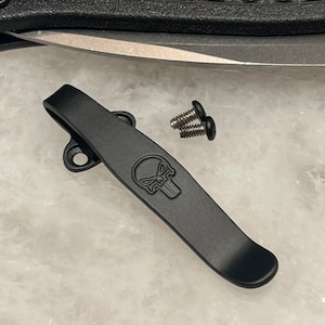 May include: Black metal pocket clip with a skull design and two screws.