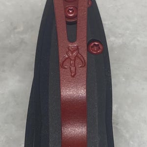 May include: A black pocket knife with a red clip and a Mandalorian symbol. The clip has three screws.