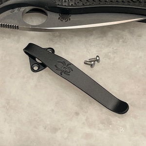 May include: Black pocket clip with a spider logo and two silver screws.