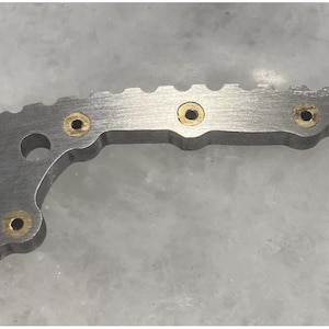May include: A silver metal object with a curved shape and a serrated edge. It has five small, round, gold-colored holes.