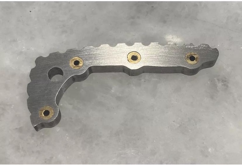 May include: A silver metal object with a curved shape and a serrated edge. It has five small, round, gold-colored holes.