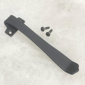 May include: A black metal handle with two screws. The handle has a curved design with a flat, elongated body and a decorative end. The screws are small and dark, complementing the handle's color.