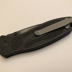 May include: Black pocket knife with a textured black handle and a silver pocket clip. The knife has the text "1070TSBW" engraved on the handle.