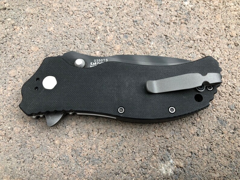 May include: Black pocket knife with a black handle and a silver pocket clip. The knife has a textured handle and a silver button on the side. The knife has the text "0350TS" and "EAR" on the side.