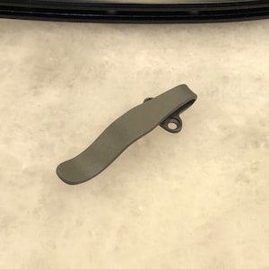 May include: A grey metal pocket clip with a curved design and two small holes.