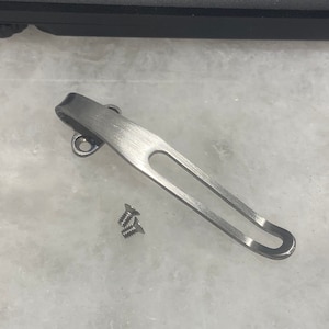 May include: A silver pocket clip with two small screws. The clip is designed to attach to a pocket knife or other tool.