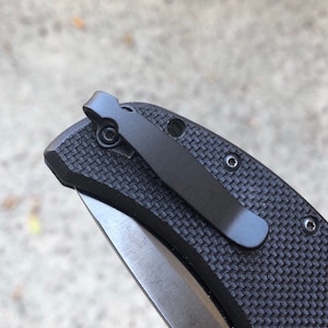 May include: Close-up of a black pocket knife with a textured handle and a black pocket clip.