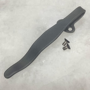 Puede incluir: Un clip de bolsillo negro mate con un diseño curvo y un pequeño agujero en la parte superior. Se incluyen dos tornillos pequeños. El clip está diseñado para sujetarse a un bolsillo u otro artículo.