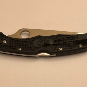 May include: A black folding knife with a silver blade and a black textured handle. The knife has a pocket clip and a Spyderco logo on the handle.
