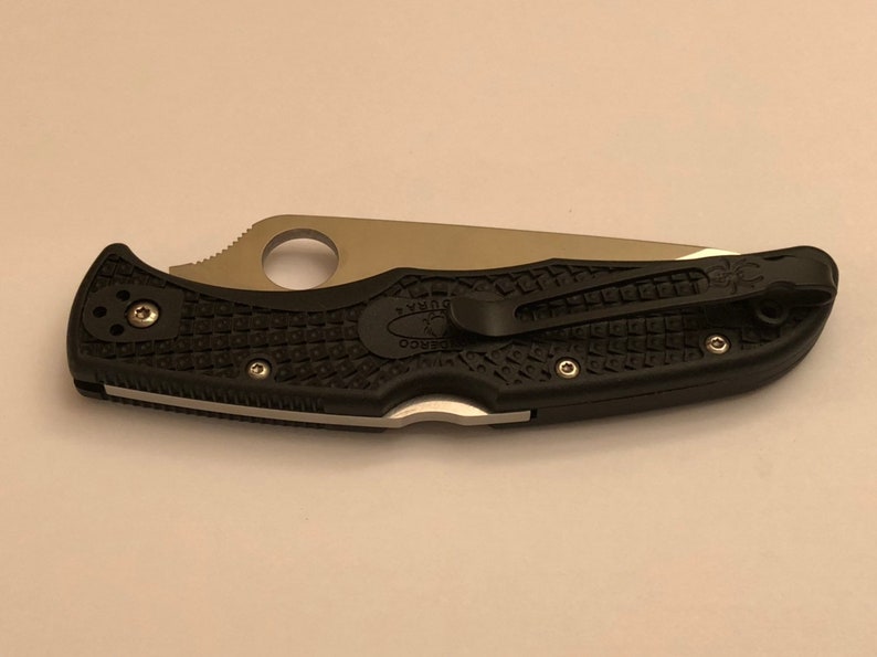 May include: A black folding knife with a silver blade and a black textured handle. The knife has a pocket clip and a Spyderco logo on the handle.