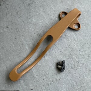 May include: A tan metal pocket clip with two holes on the top and one on the side. Three black screws are included.