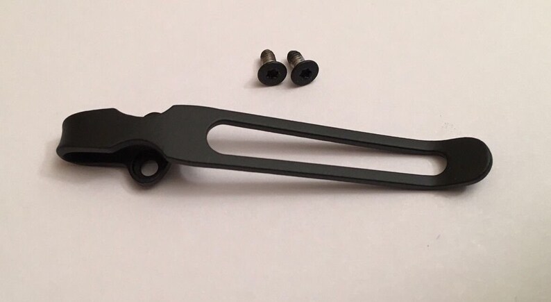 May include: A black metal pocket clip with a rounded end and a small hole on the side. Two small black screws are included.