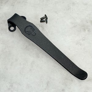May include: Black metal pocket clip with a skull design and two screws.