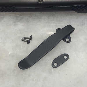 May include: A black metal pocket clip with two small screws and a separate black metal loop. The clip is designed to attach to a pocket or belt.