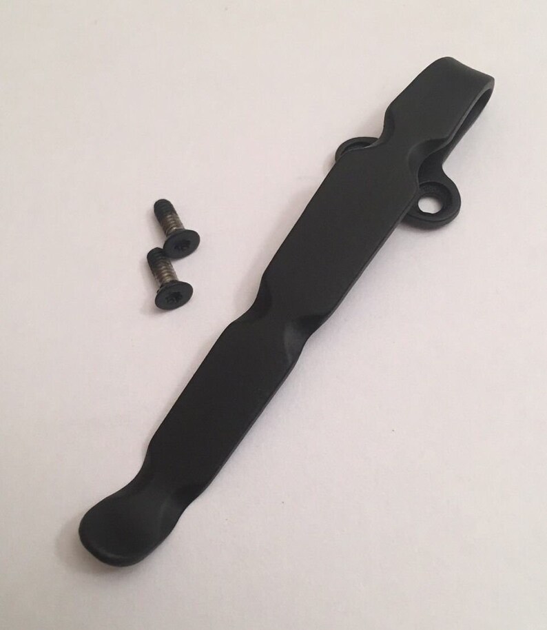 May include: Black metal pocket clip with two small screws. The clip has a curved design and a hole at the top.
