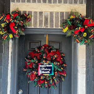 May include: A black door with a wreath made of red, green, and yellow mesh with a sign that says "Happy Black History Month". There are two smaller wreaths on either side of the door.