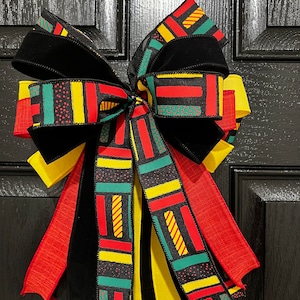 May include: A black velvet bow with red, yellow, and green patterned ribbon. The ribbon has a geometric design with stripes and dots.