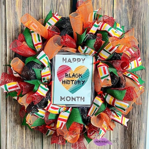 May include: A black mesh wreath decorated with red, orange, green, and yellow ribbon. The wreath has a sign that reads "Happy Black History Month" with a colorful heart graphic.