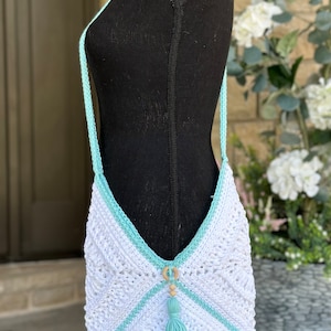 Puede incluir: Bolso de crochet blanco con ribete azul claro y borla. El bolso tiene un acento de cuentas de madera y anillo.