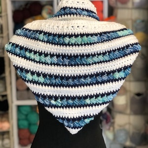 May include: A white and blue crocheted triangular scarf with a textured design. The scarf is displayed on a black mannequin.