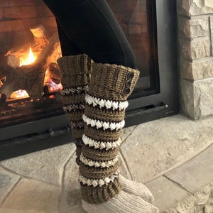 Puede incluir: Un par de polainas de crochet marrón y blanco con cierre de botón. Las polainas se llevan sobre un par de calcetines grises.