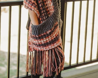 May include: A crocheted shawl with a fringe border in shades of pink, orange, and brown. The shawl has a large pocket on the front.