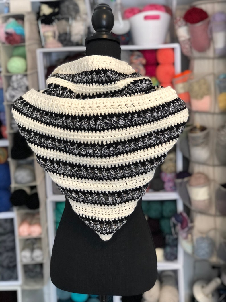 May include: A black and white striped crocheted infinity scarf with a textured design. The scarf is displayed on a black mannequin.