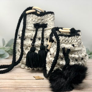 May include: Two crocheted drawstring bags with black trim and black tassels. The larger bag has a long black strap. Both bags have black beads and a white background.